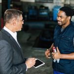 Happy black mechanic communicating with his manager in auto repair shop.
